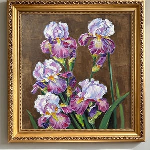 May include: An oil painting of purple and white iris flowers with green stems and leaves against a dark brown background, enclosed in an ornate gold-coloured frame with a decorative embossed pattern along the edges of the rectangular border.