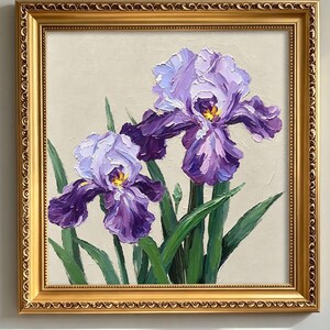 May include: An oil painting of two purple iris flowers with thick, textured brushstrokes, green stems, and yellow centres, set against a neutral beige background and enclosed in an ornate, metallic gold-coloured rectangular frame.