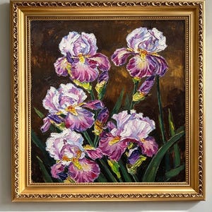 May include: An oil painting of purple and white iris flowers with yellow centres and green stems, rendered with thick, visible brushstrokes. The floral arrangement is set against a dark brown background and enclosed in an ornate gold frame.