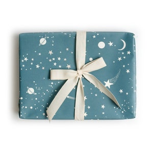 Peut inclure: Une boîte cadeau bleue avec un ruban blanc et un motif sur le thème de l'espace avec des étoiles, des planètes et une comète. Le motif est répété sur tous les côtés de la boîte.