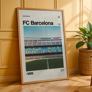 Puede incluir: Un póster enmarcado con el logotipo del FC Barcelona y una vista del estadio. El póster, en un marco de madera, muestra el nombre del equipo en negro. Se ven las gradas del estadio, con el texto "MES QUE UN CLUB" en amarillo.