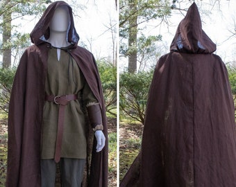 May include: A brown hooded cloak with a matching cape, displayed on a mannequin. The cloak features a pointed hood and a long, flowing design. The mannequin is also wearing a green tunic, brown belt, and gray pants.