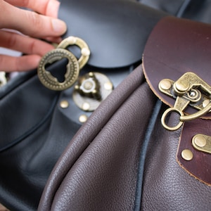 May include: Two leather bags with metal clasps and buckles. One bag is black and the other is brown.