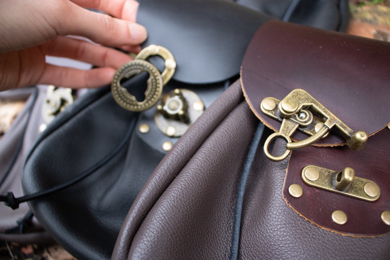 May include: Two leather bags with metal clasps and buckles. One bag is black and the other is brown.