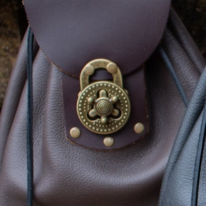 May include: A brown leather bag with a decorative brass clasp. The clasp has a circular design with a central star and a ring.