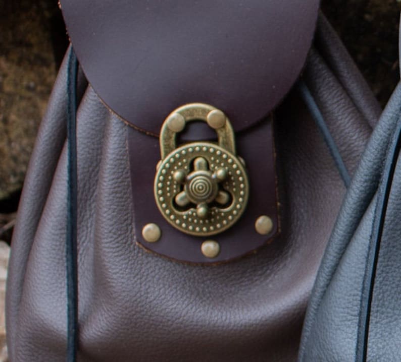 May include: A brown leather bag with a decorative brass clasp. The clasp has a circular design with a central star and a ring.