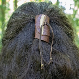 May include: A brown leather hair tie with a bone accent and two small metal beads on the ends of the ties.