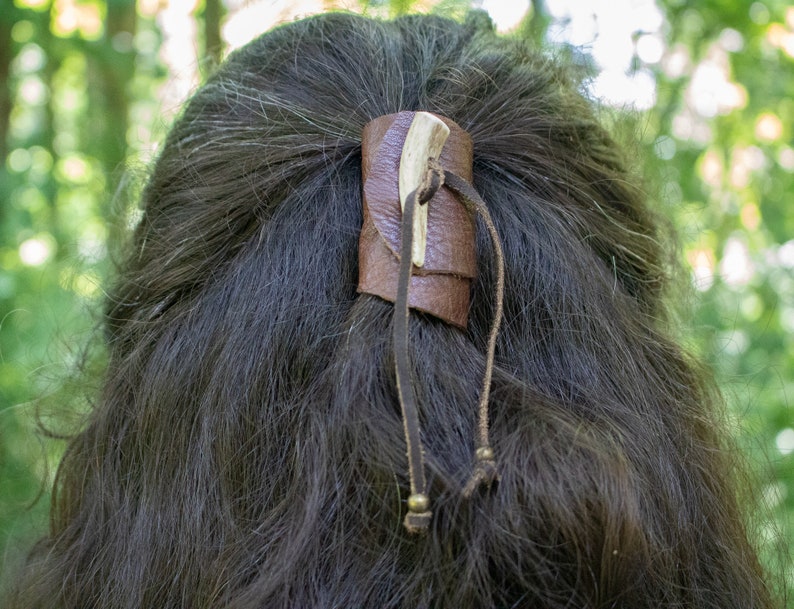 May include: A brown leather hair tie with a bone accent and two small metal beads on the ends of the ties.