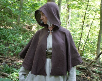 May include: A brown hooded cloak with a simple design. The cloak is made of a soft, natural fabric and has a drawstring hood. The cloak is worn over a light-colored garment.