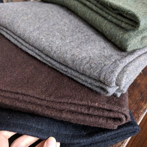 May include: Four wool blankets stacked on top of each other. The top blanket is green, the next is gray, the next is brown, and the bottom blanket is black.