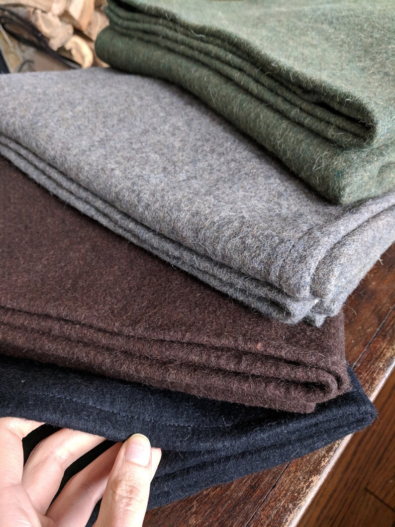 May include: Four wool blankets stacked on top of each other. The top blanket is green, the next is gray, the next is brown, and the bottom blanket is black.