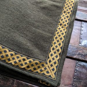 May include: A green fabric throw blanket with a gold and black Celtic knot border.