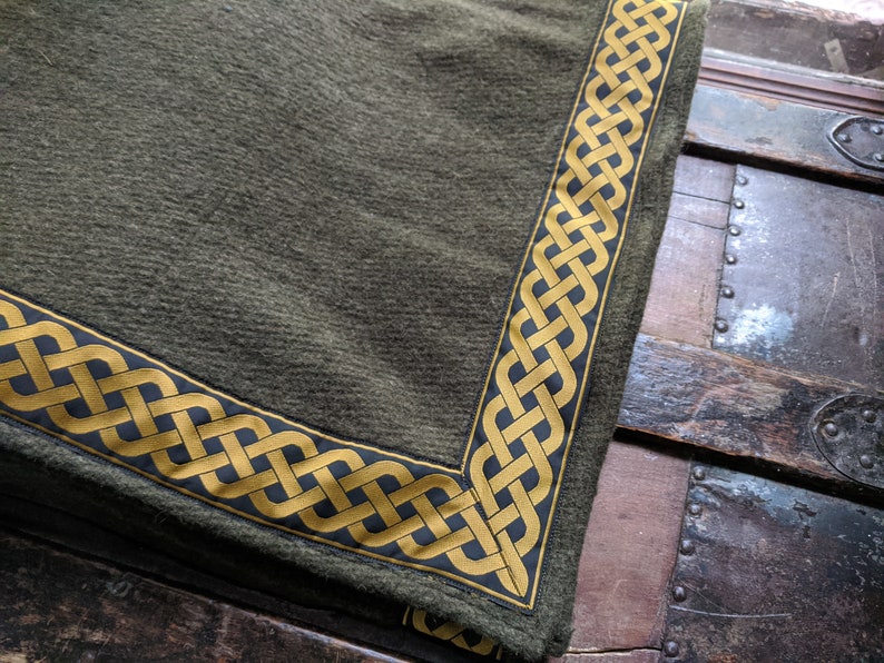 May include: A green fabric throw blanket with a gold and black Celtic knot border.
