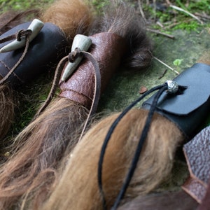 May include: Three leather wrapped bundles of hair with bone or antler tips. The bundles are tied with leather cords and have decorative metal accents.