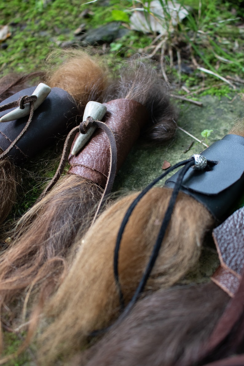 May include: Three leather wrapped bundles of hair with bone or antler tips. The bundles are tied with leather cords and have decorative metal accents.
