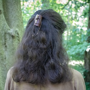 May include: A brown leather hair clip with a bone accent. The clip is worn in a person's hair.