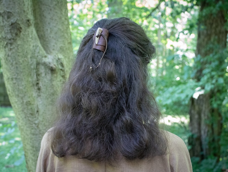 May include: A brown leather hair clip with a bone accent. The clip is worn in a person's hair.