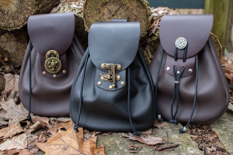 May include: Three leather pouches with different closures. The pouch on the left has a round metal clasp with a decorative design. The middle pouch has a metal buckle with a flap. The pouch on the right has a round metal Celtic knot design.