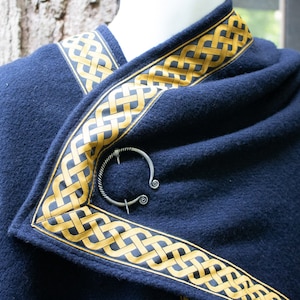May include: A navy blue shawl with a gold Celtic knot trim and a silver ring brooch.