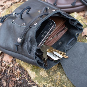 May include: A black leather pouch with a drawstring closure, open to reveal a cell phone, wallet, and keys inside.