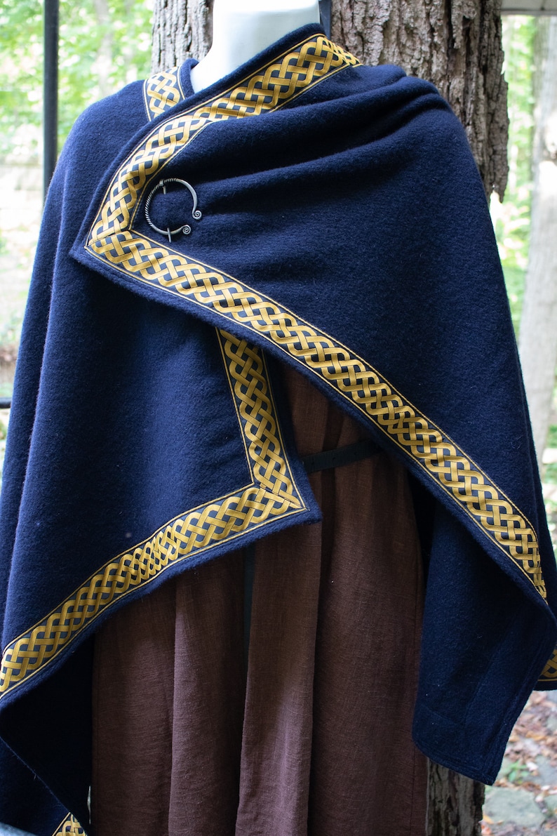 May include: A dark blue wool cloak with a gold Celtic knot trim. The cloak is fastened with a silver ring brooch.