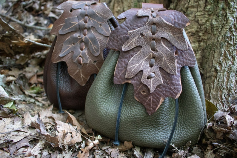 May include: Two leather pouches with a leaf design. The pouches are brown and green and have a drawstring closure.