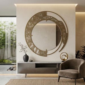 Op de afbeelding: Een grote ronde wandspiegel met een ingewikkeld goudkleurig metalen frame met een opengewerkt rasterontwerp. De spiegel is boven een lage, rechthoekige donkergrijze consoletafel gemonteerd en vormt een blikvanger in de kamer.