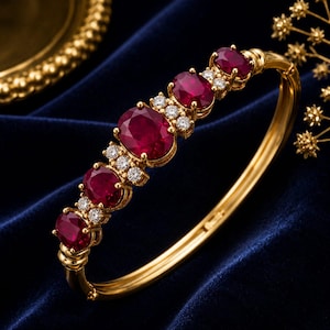 Peut inclure: Un bracelet jonc articulé en or orné de quatre rubis rouge foncé taille ovale et de petits diamants blancs ronds disposés en ligne. Le bracelet présente un anneau en or poli et un fermoir sécurisé, créant un contraste vif entre les pierres.