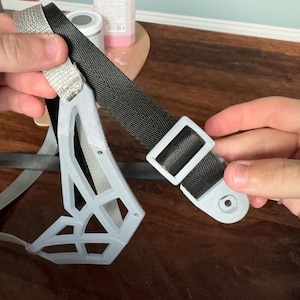 May include: A light gray 3D-printed geometric frame attached to a black nylon strap with a matching light gray plastic slider buckle. The frame features an open-work lattice design with small circular holes at the ends for attachment points.