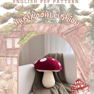 May include: A crochet mushroom cushion with a deep red cap featuring white spots and a cream-colored stem. The image includes the text ENGLISH PDF PATTERN MUSHROOM CUSHION, a green caterpillar illustration, and a cabin background.