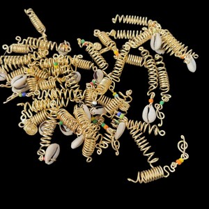 May include: Gold-colored hair coils with spiral designs, adorned with small seashells and colorful beads. The coils are arranged against a black background, creating a striking contrast. These hair accessories add a unique touch to any hairstyle.