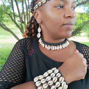 May include: A full jewellery set made from natural seashells. The set includes a headband, earrings, a choker necklace, and a bracelet. The shells are white with brown markings, set against black string and gold-coloured earring hooks.