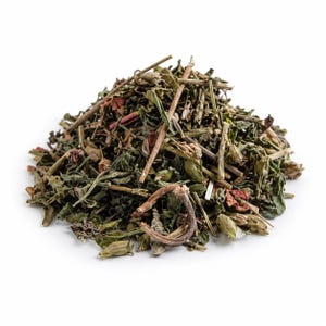 May include: A close-up of a pile of dried herbal tea leaves and stems, with a mix of green, brown, and reddish hues. The tea blend appears to be a mix of different botanicals. The image is set against a plain white background.