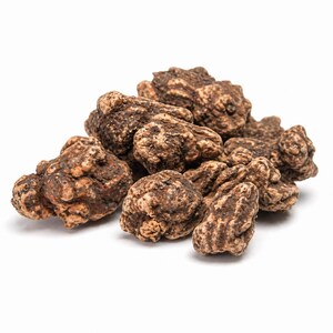 Peut inclure: Un tas de morceaux de racine de maca brun foncé de forme irrégulière. Les morceaux ont une surface rugueuse et texturée avec des taches brun clair et beige. Les racines de maca sont sur fond blanc.