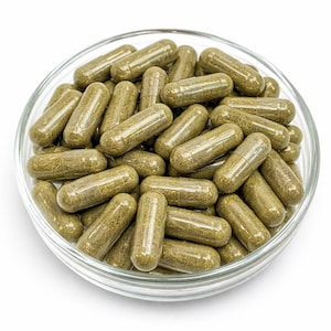 Può includere: Una ciotola di vetro trasparente piena di numerose capsule verdi. Le capsule hanno un involucro traslucido, che rivela una sostanza verde e granulare all'interno. La ciotola è posta su uno sfondo bianco, evidenziando il colore e la consistenza delle capsule.