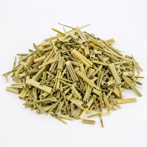 May include: A close-up of a pile of dried lemongrass stalks, showing varying shades of green and tan. The stalks are cut into short lengths and have a natural, textured appearance. The image is set against a plain white background, highlighting the plant material.