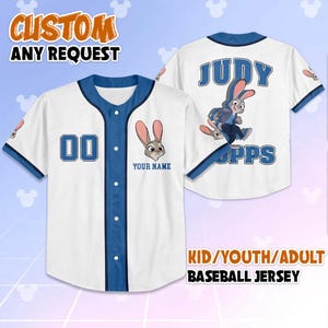 May include: White baseball jersey with blue trim and buttons. Features a cartoon rabbit graphic and the text "YOUR NAME" below it. The jersey also has the number "00" on the front and "JUDY HOPPS" on the back. The text "CUSTOM ANY REQUEST" is at the top.
