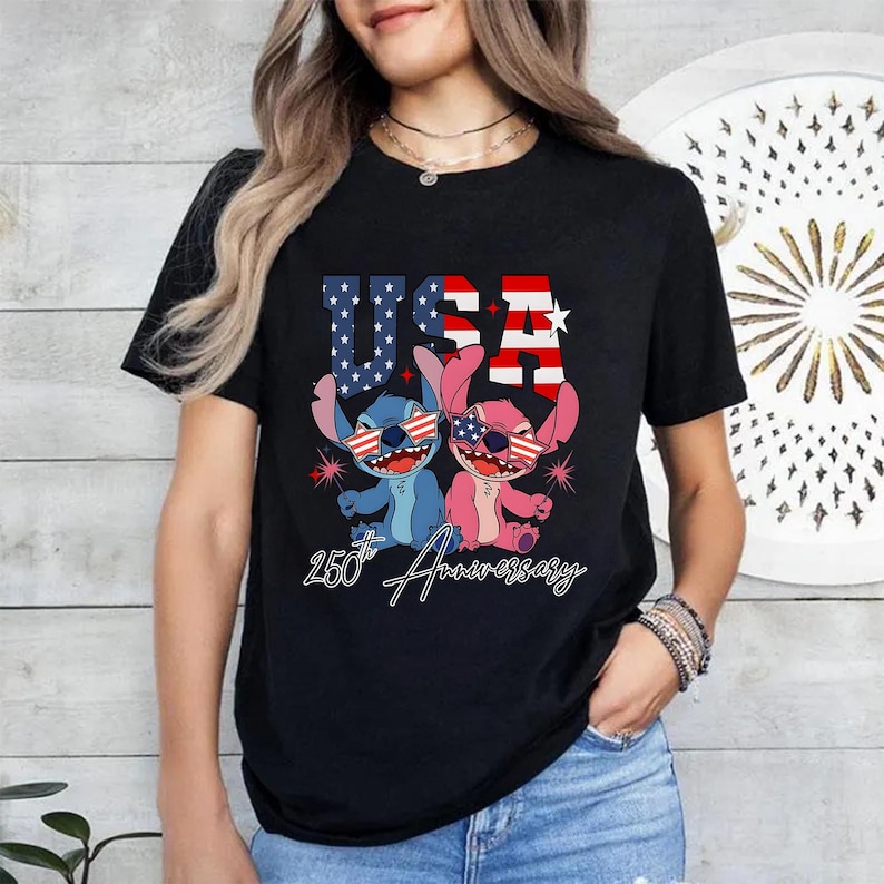 May include: Black t-shirt with a graphic of two cartoon characters wearing sunglasses with the American flag design. The word "USA" is above the characters, and "250th Anniversary" is written below.