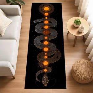 Könnte beinhalten: Schwarzer rechteckiger Teppich mit einer detaillierten Schlange in Orange und Gold. Das Schlangendesign ist zentral, mit orangefarbenen Kugeln entlang des Körpers. Der Teppich liegt auf einem Holzboden. Spirituelles Thema.