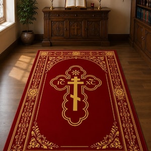 May include: A rectangular red rug with a gold Orthodox cross design in the center. The rug has a gold floral border and is placed on a wooden floor. The room also features a wooden cabinet, religious icons, and candles.