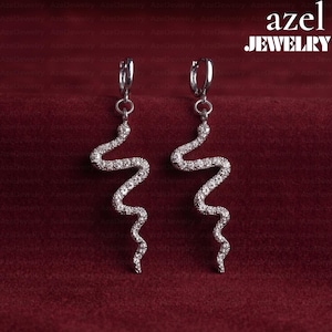 May include: A pair of silver-toned hoop earrings featuring dangling, snake-shaped pendants encrusted with small, clear, sparkling stones. The text 'azel JEWELRY' is visible in the upper right corner of the image, set against a deep red background.