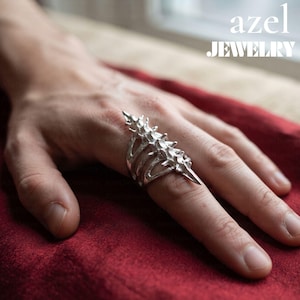 May include: A silver ring with a textured, segmented design resembling a spinal column, featuring pointed protrusions along the top. The text 'azel JEWELRY' is visible in the upper right corner of the image.