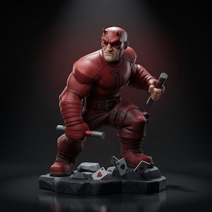 Puede incluir: Una figura roja de Daredevil en posición de combate agachada, con un traje texturizado, máscara con cuernos y dos bastones de puntas plateadas. El personaje se apoya sobre una base rocosa oscura con varias cartas de juego esparcidas.