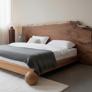 May include: A wooden bed frame with a live edge headboard. The bed is made with light-colored wood and has a gray blanket and white bedding. The bed sits on a white rug. A lamp and curtains are visible in the background.