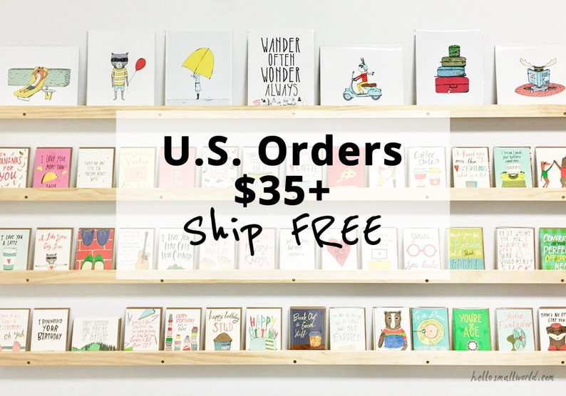 May include: A shelf display of greeting cards with various illustrations and text. The cards are arranged in three rows. The text on the sign reads "U.S. Orders $35+ Ship FREE".