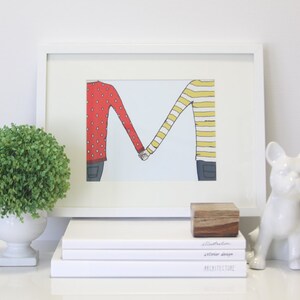 May include: A white framed illustration of two people holding hands, forming the letter "M". The person on the left is wearing a red sweater with white polka dots, and the person on the right is wearing a yellow and white striped sweater. The illustration is on a white background.