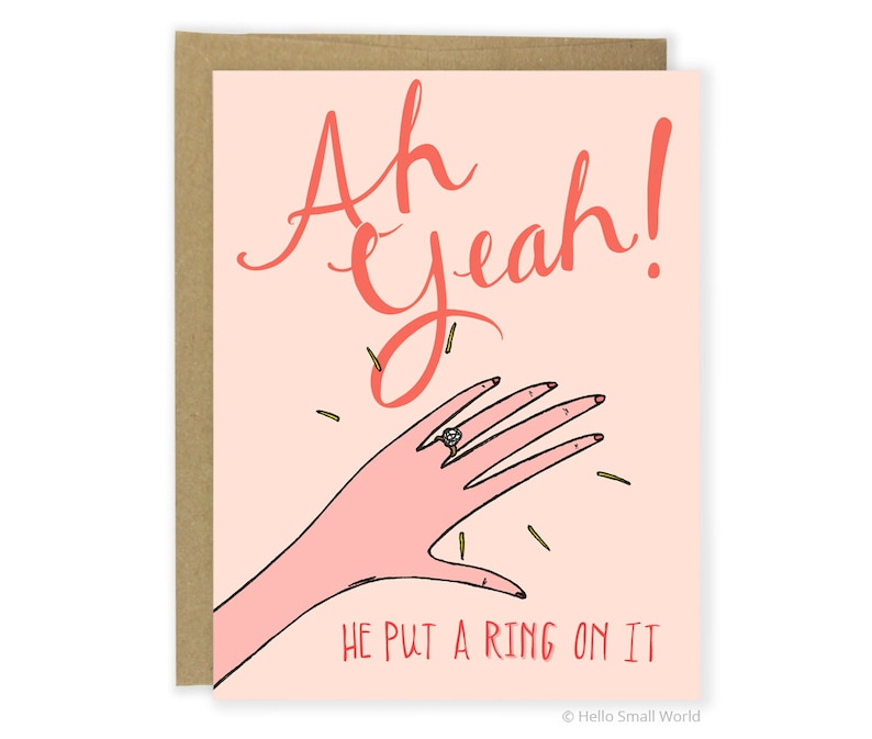 Puede incluir: Una tarjeta rosa con el texto "Ah Yeah!" en letra roja. Se muestra una mano de dibujos animados con un anillo de diamantes en el dedo anular con confeti a su alrededor. El texto "He put a ring on it" est&aacute; debajo de la mano.
