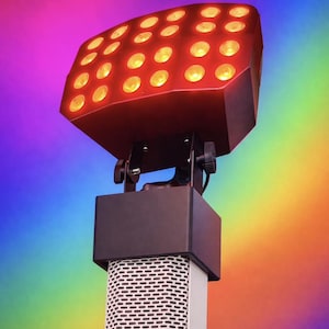 May include: A red stage light with multiple yellow bulbs, mounted on a black and silver stand. The light fixture has a rectangular shape with rounded corners. The background is a rainbow gradient.