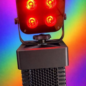 May include: A black stage light with four red LED lights. The light is mounted on a black stand with a honeycomb grill. The background is a gradient of rainbow colors.