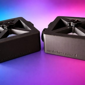 May include: Two black audio equipment stands, each with the text "northshore sound". They feature a triangular top with a central knob and a side adjustment knob. The background gradient shifts from blue to purple.